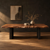 Live edge slab dining table on two open rectangular block legs in a dark studio against a charcoal plaster wall