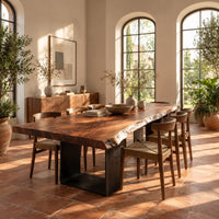 Live edge slab dining table on two open rectangular block legs in a bright dining room with arched windows and plants