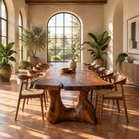 Live edge dining table with a thick top and a sculpted arched base in a bright dining room with arched windows and plants