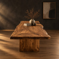 Live edge dining table with a swirling grain top on one block base in a dark studio against a charcoal plaster wall