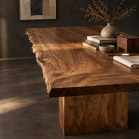 Corner detail of live edge dining table with a swirling grain top on one block base beside wood, brass and linen samples