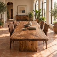 Live edge dining table with a swirling grain top on one block base in a bright dining room with arched windows and plants