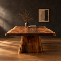 Live edge dining table with a thick slab top and tapered block base in a dark studio against a charcoal plaster wall