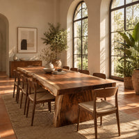 Live edge dining table with a thick slab top and tapered block base in a bright dining room with arched windows and plants