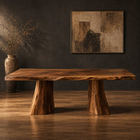 Dining table with a thick live edge slab top on two flared pedestal legs in a dark studio against a charcoal plaster wall
