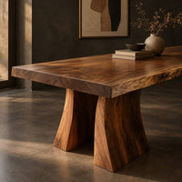 Corner detail of dining table with a thick live edge slab top on two flared pedestal legs beside wood, brass and linen samples