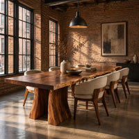 Dining table with a thick live edge slab top on two flared pedestal legs in an industrial loft dining room with exposed brick