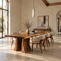 Dining table with a thick live edge slab top on two flared pedestal legs in a bright open plan dining room