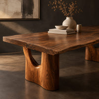 Corner detail of long dining table with a live edge top and two arched pedestal legs beside wood, brass and linen samples