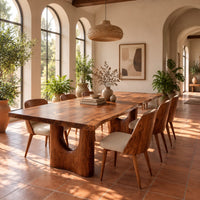 Long dining table with a live edge top and two arched pedestal legs in a bright dining room with arched windows and plants