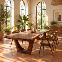 Live edge wooden dining table on two arched pedestal legs in a bright dining room with arched windows and plants