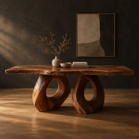 Rectangular dining table with a live edge slab top and two loop pedestals in a dark studio against a charcoal plaster wall