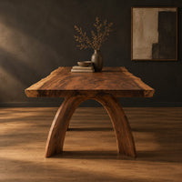 Live edge dining table with a thick slab top and two arched legs in a dark studio against a charcoal plaster wall
