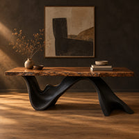 Live edge desk with a dark sculpted wave shaped base in a dark studio against a charcoal plaster wall