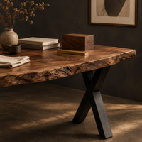 Corner detail of live edge desk with a natural slab top and black crossed legs beside wood, brass and linen samples