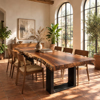 Live edge slab dining table on two dark squared frame legs in a bright dining room with arched windows and plants