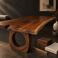 Corner detail of long live edge slab dining table on thick ring shaped bases beside wood, brass and linen samples