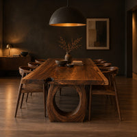 Long live edge slab dining table on thick ring shaped bases in a dark dining room at golden hour