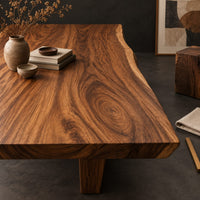 Corner detail of thick wooden slab table top with a wavy natural edge and swirling grain beside wood, brass and linen samples