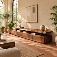 Long low tv stand with a natural edge slab top over a block base in a bright living room with arched windows and plants