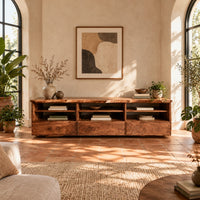 Live edge tv stand with three open shelf bays and lower front panels in a bright living room with arched windows and plants