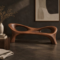 Corner detail of long wood bench with a pinched middle and two oval openings beside wood, brass and linen samples