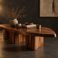 Corner detail of leaf shaped coffee table with a pointed slab top on three chunky block legs beside wood, brass and linen samples