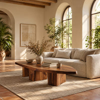 Leaf shaped coffee table with a pointed slab top on three chunky block legs in a bright living room with arched windows and plants
