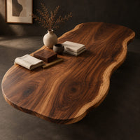 Corner detail of long freeform wood table top with rippling live edge sides and warm grain beside wood, brass and linen samples