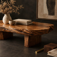Corner detail of long oval coffee table with a raw edged slab top on two block legs beside wood, brass and linen samples