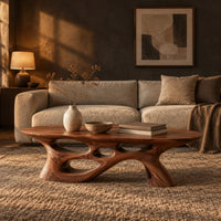 Long oval coffee table with a sweeping cutout base in a dark living room at golden hour