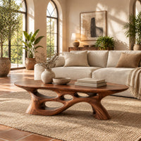 Long oval coffee table with a sweeping cutout base in a bright living room with arched windows and plants