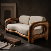 Corner detail of sofa with a sculpted wood frame, open loop arms and a long seat cushion beside wood, brass and linen samples