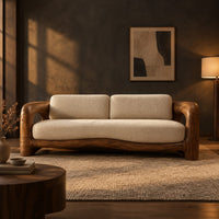 Sofa with a sculpted wood frame, open loop arms and a long seat cushion in a dark living room at golden hour