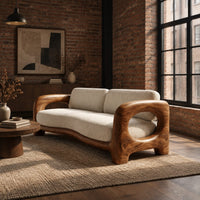 Sofa with a sculpted wood frame, open loop arms and a long seat cushion in an industrial loft living room with exposed brick