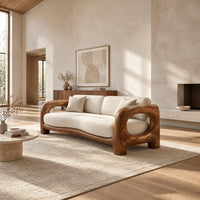 Sofa with a sculpted wood frame, open loop arms and a long seat cushion in a bright open plan living room