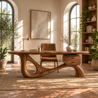 Desk with an oval top, a looped sculpted base and a two drawer box in a bright home office with arched windows and plants