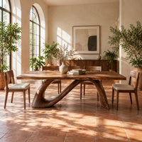 Dining table with a sweeping ribbon base that folds into an open loop in a bright dining room with arched windows and plants