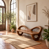 Bench with a flat plank seat, looped arms and ring shaped legs in a bright entryway with arched windows and plants