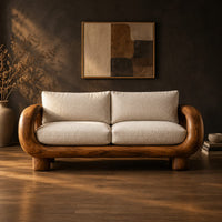 Sofa with thick looped wood arms, chunky block legs and cream cushions in a dark studio against a charcoal plaster wall