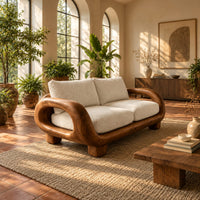 Sofa with thick looped wood arms, chunky block legs and cream cushions in a bright living room with arched windows and plants