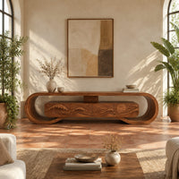 Tv stand inside a looped wooden frame with an ocean wave carved front in a bright living room with arched windows and plants