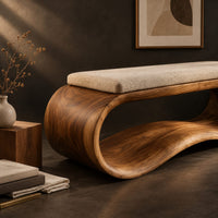 Corner detail of wooden bench made from a looped ribbon frame with a slim cream cushion beside wood, brass and linen samples
