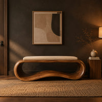 Wooden bench made from a looped ribbon frame with a slim cream cushion in a dark entryway at golden hour