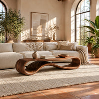 Coffee table with a flat top over a looping wave shaped wooden base in a bright living room with arched windows and plants