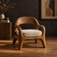 Accent chair with looping arms, an open scooped back and a soft seat cushion in a dark studio against a charcoal plaster wall