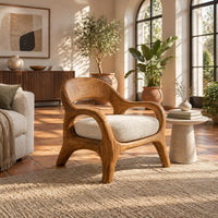 Accent chair with looping arms, an open scooped back and a soft seat cushion in a bright living room with arched windows and plants