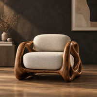 Armchair with looping carved wood arms and plush cream cushions in a dark studio against a charcoal plaster wall