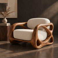 Corner detail of armchair with looping carved wood arms and plush cream cushions beside wood, brass and linen samples