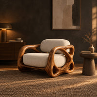 Armchair with looping carved wood arms and plush cream cushions in a dark living room at golden hour